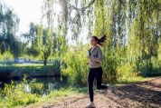 Junge Frau joggt bei Frühlingswetter auf einer Finnenbahn am Fluss entlang Junge Frau joggt bei Frühlingswetter auf einer Finnenbahn am Fluss entlang